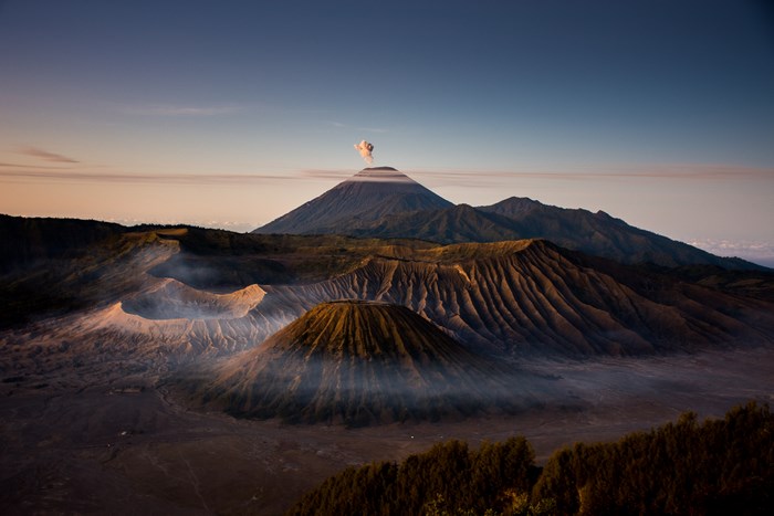 Volcano erupting smoke at sunrise with misty craters