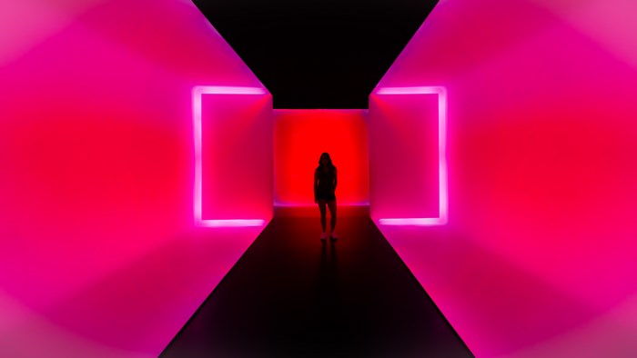 Person standing in a pink and red neon tunnel