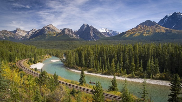 Train tracks by a river with mountains and forest
