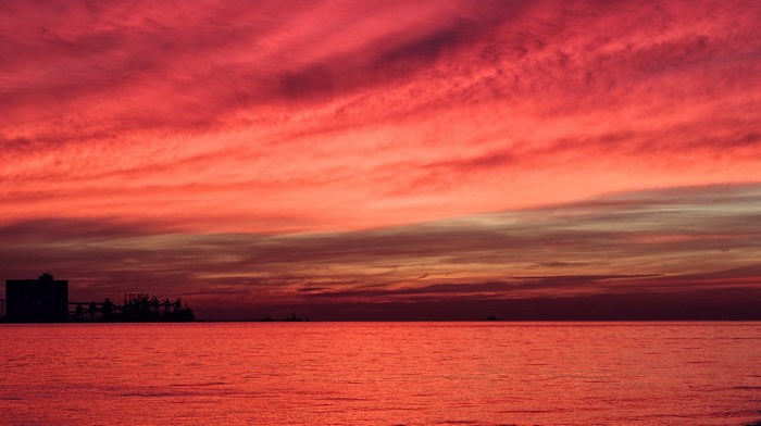Red sky over the ocean at sunset with a port