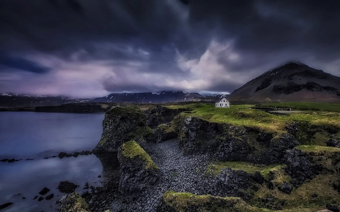 White house on a grassy hill by the sea in Iceland