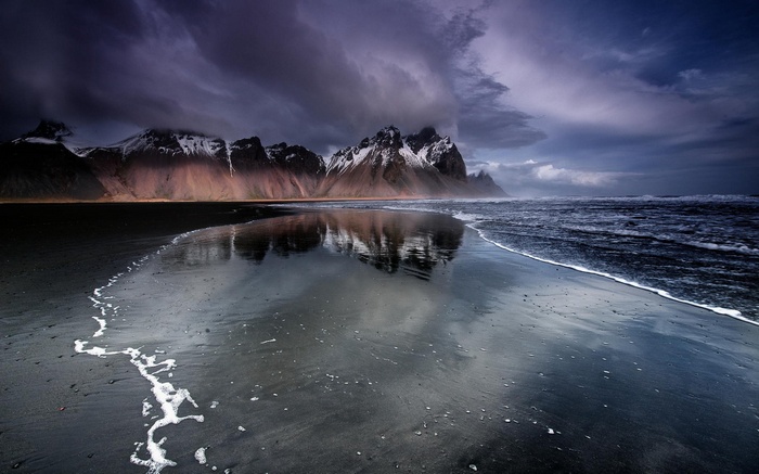 Black sand beach with mountains and ocean reflection