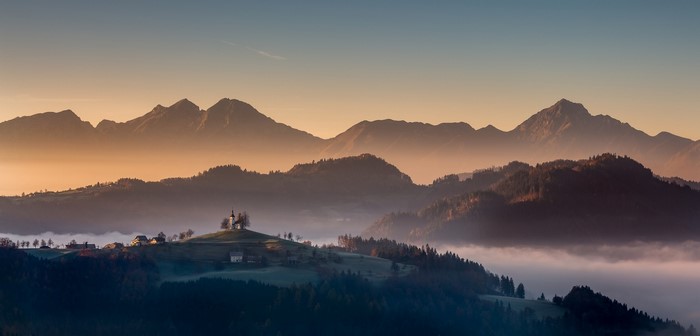 Sunrise over mountains with a village and church in Slovenia