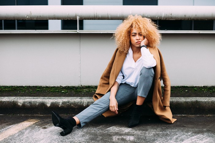 Woman with blonde curly hair sitting on pavement