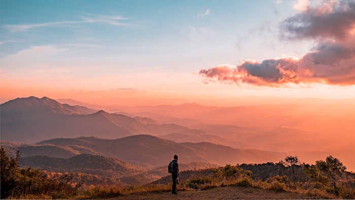 Man standing on mountain overlooking landscape at sunset