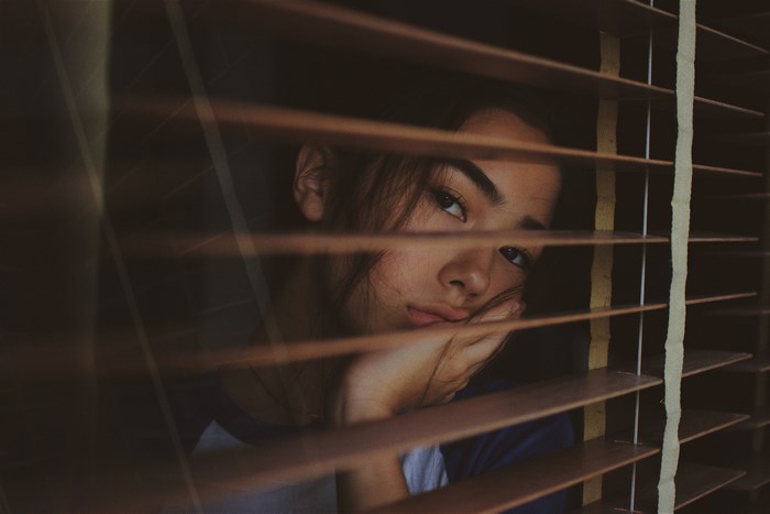 Woman resting her head on her hand behind blinds
