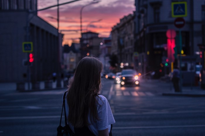 Woman standing at a city street crossing at sunset