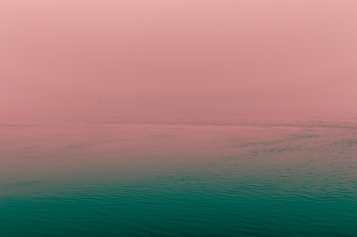 Pink fog over a calm green ocean with a distant sail