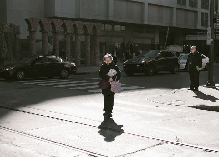 Elderly woman crossing street with bags