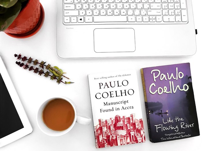 Paulo Coelho books on a desk with a laptop and tea