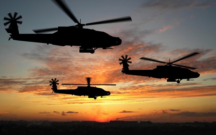Three AH-64 Apache helicopters silhouetted at sunrise