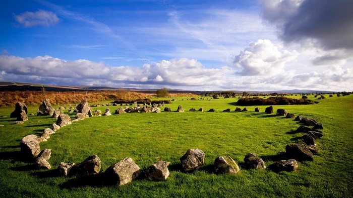 Ancient stone circle on a grassy field under a cloudy sky