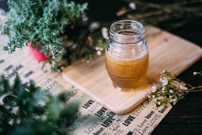 Jar of honey on a wooden board with plants