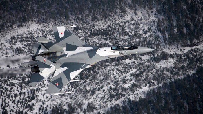 Sukhoi Su-35 fighter jet flying over a snowy forest