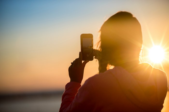 Woman taking a photo of the sunset with a smartphone