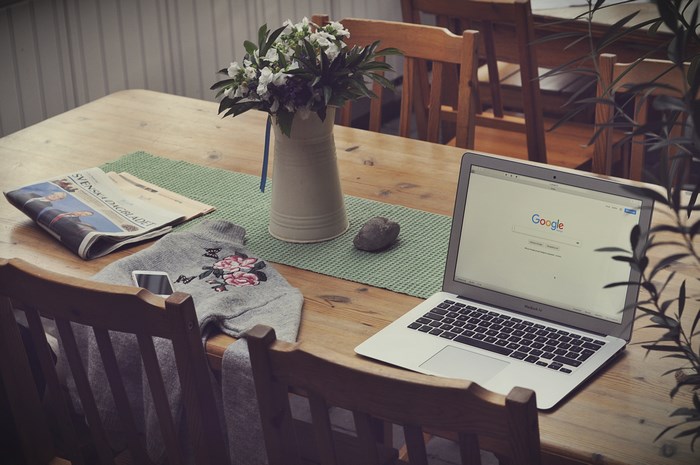 Laptop with Google search on a wooden table with newspaper and flowers