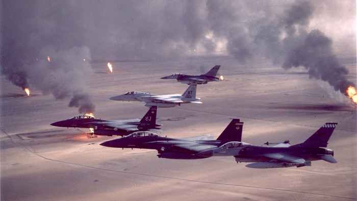 F-15 and F-16 fighter jets fly over burning oil wells