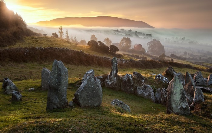 Misty morning sunrise over ancient stone circle in rolling hills
