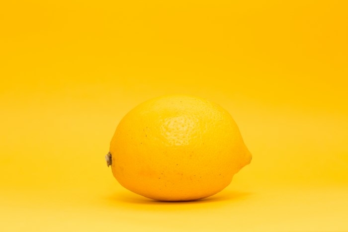 A single yellow lemon on a bright yellow background