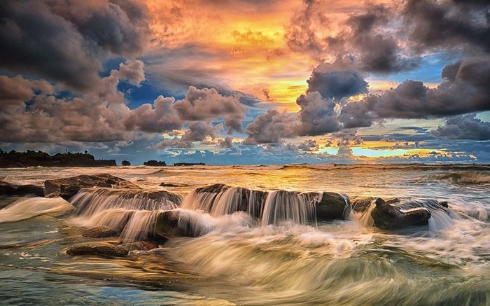 Sunset over rocky coast with waves in Bali, Indonesia