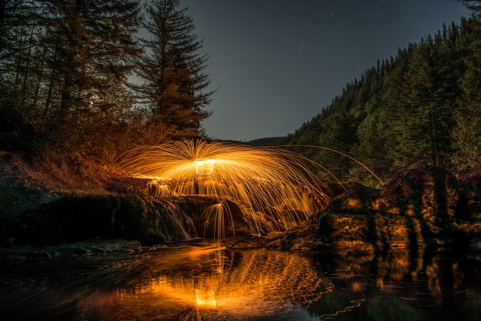 Steelwool fire spinning over a waterfall at night
