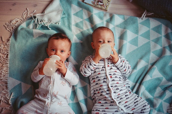 Two babies drinking from bottles on a blanket