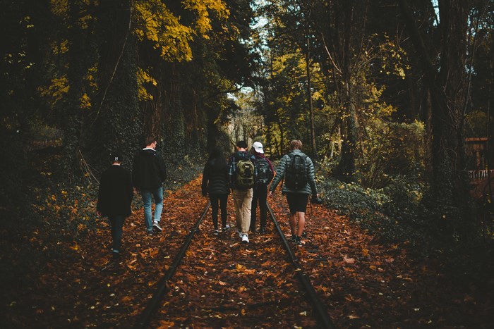 Group of friends walking on train tracks in autumn forest