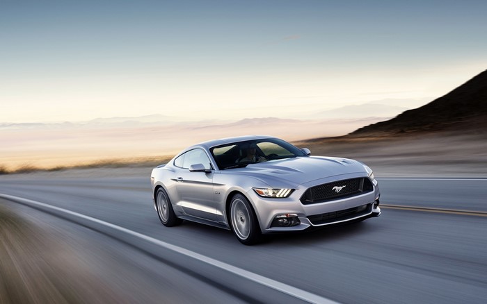 Silver Ford Mustang GT driving on a road at sunset