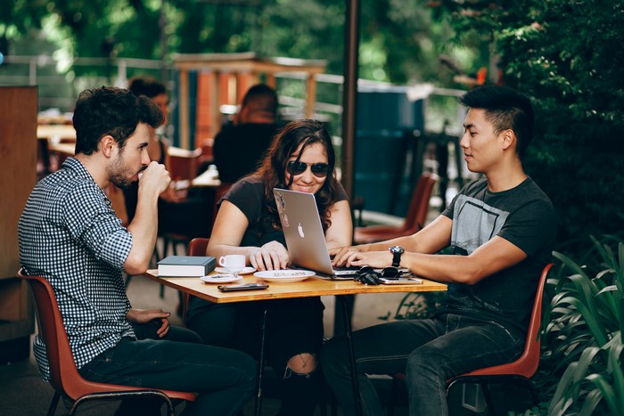 Three people working on a laptop at a cafe