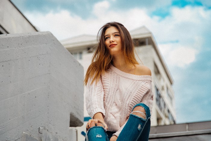 Woman in pink sweater and ripped jeans sitting on stairs