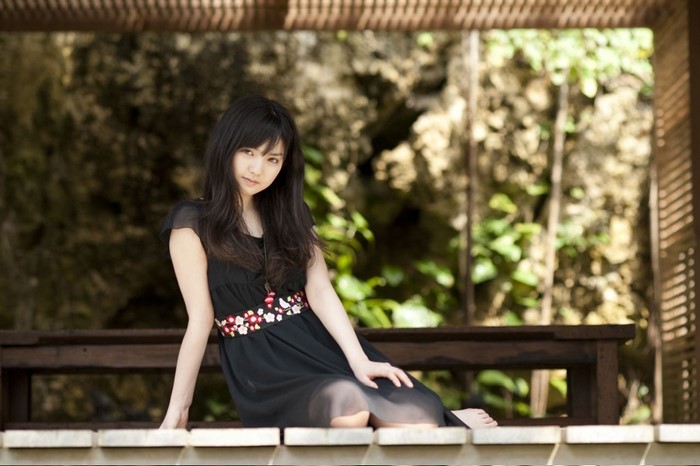 Sayumi Michishige sitting on a wooden bench outdoors