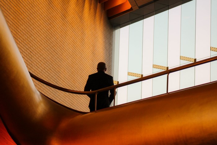 Man in Suit on Escalator with Orange Walls
