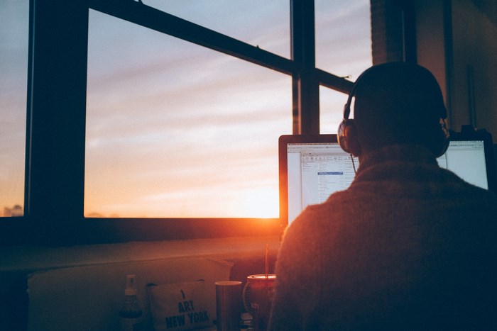 Man working on computer with headphones at sunset