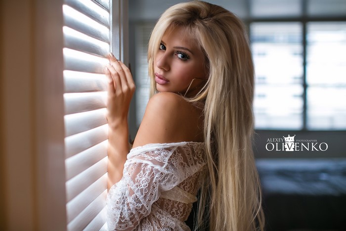 Woman with long blonde hair by window blinds