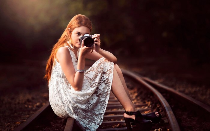 Woman with red hair holding a camera on train tracks