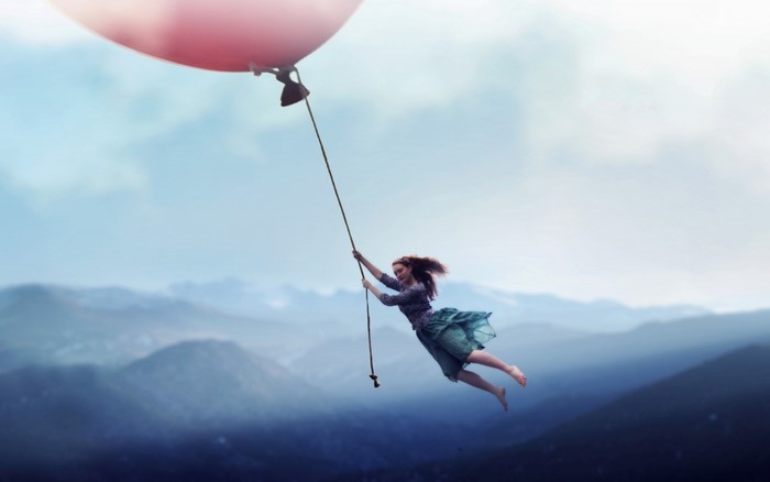Woman holding onto a balloon flying over mountains