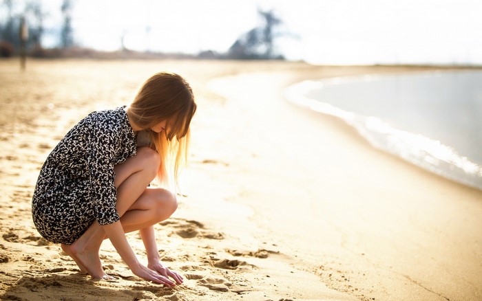 Woman crouching on a sandy beach near the ocean