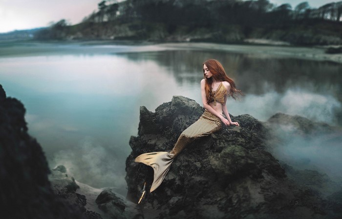 Fantasy art of a mermaid on rocks by the water