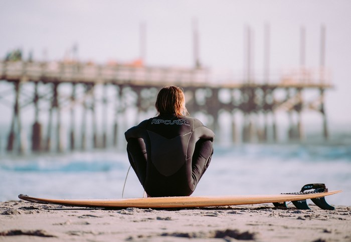 Surfer in wetsuit sitting on surfboard on beach