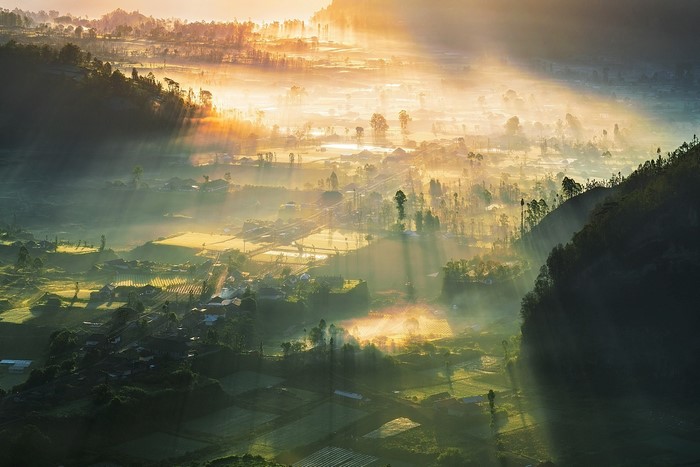 Sunrise over a misty valley village with sunbeams