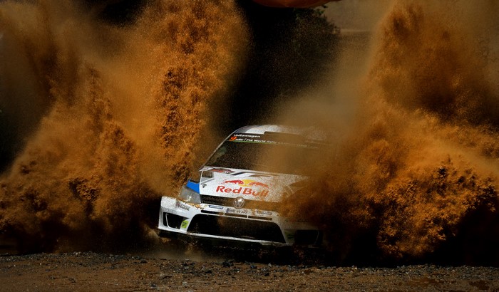Volkswagen rally car driving through dirt and dust