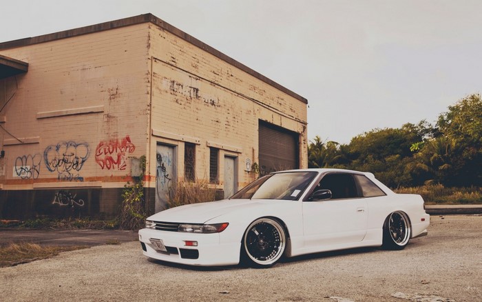 White Nissan Silvia S13 parked by graffiti-covered building