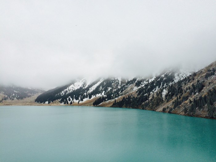 Turquoise lake and misty mountains with pine trees