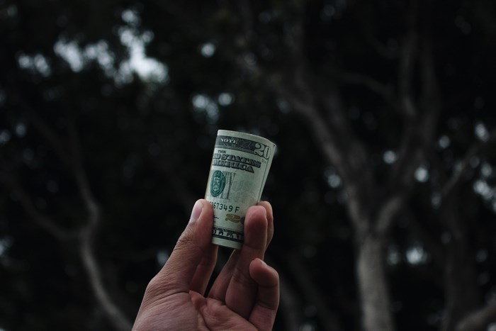 Hand holding a rolled up twenty dollar bill