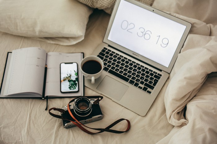 MacBook, iPhone, Camera, and Planner on a Bed