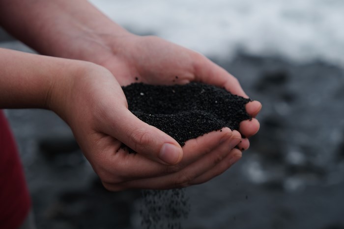 Hands holding black volcanic sand on a beach