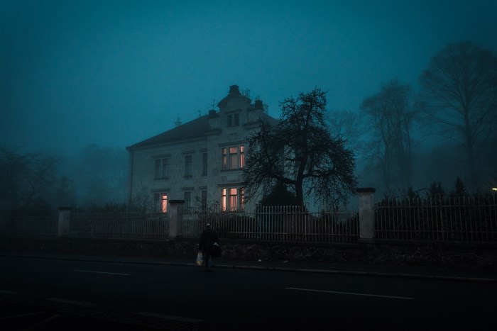 Man walking past a foggy house at night