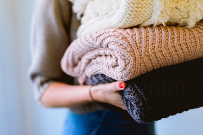 Woman holding a stack of folded knitted sweaters