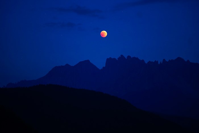 Red moon eclipse over silhouette mountains in Italy