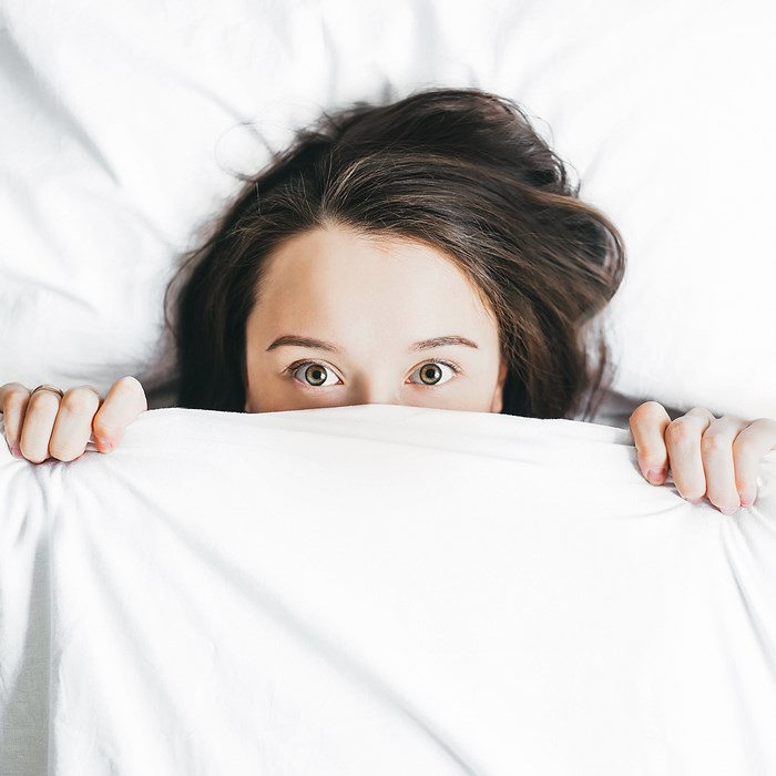 Woman hiding under white sheets in bed